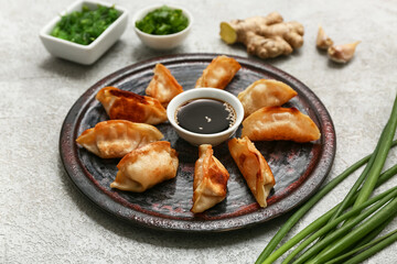 Plate with fried Japanese gyoza and bowls of seaweed salad and green onion on grey background