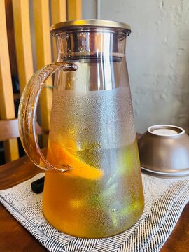 木製テーブルの上のガラスポットに入ったオレンジ入りフルーツウォーター（Fresh fruit water with orange in a glass pot on wooden table）