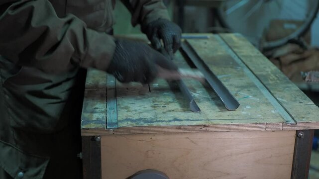 Workshop. A worker removes burrs from a sawn pipe that is on a workbench.