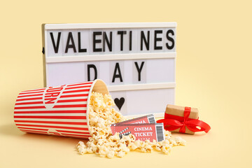 Board with text VALENTINE'S DAY, bucket of popcorn, cinema tickets and gift box on yellow background