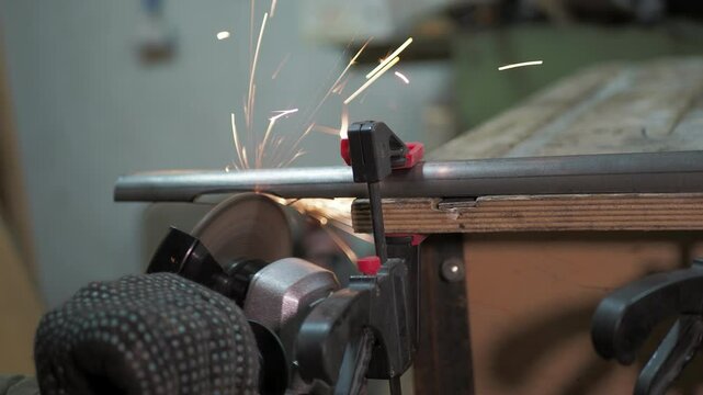 Workshop. A worker removes a layer of metal from a pipe that is clamped to a workbench using a angle grinder.