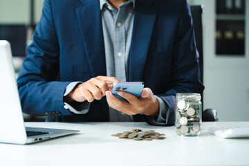 businessman holding coins putting in glass with using smartphone and calculator to calculate...
