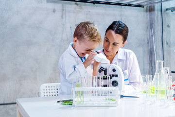 A young boy and female scientist explore plant samples under a microscope in a lab, learning...