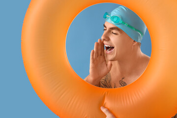 Handsome male swimmer with inflatable ring telling something on blue background