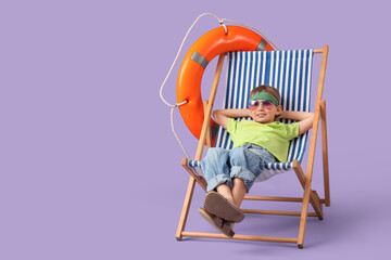 Cute little boy sitting in deck chair with lifebuoy ring on lilac background. Travel concept