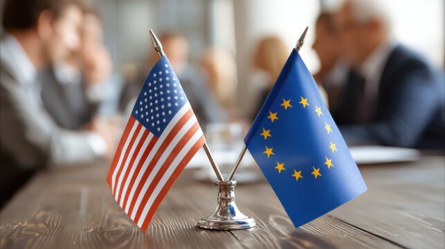 Close-up of USA and European Union flags crossed on a meeting table, symbolizing international relations, diplomacy, and cooperation. Blurred business professionals in the.