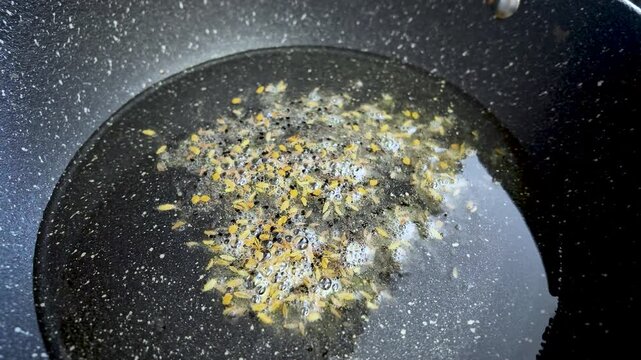 Cumin seeds sizzling in hot oil within a pan during food preparation. slow motion