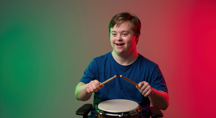 Smiling boy with down syndrome holding drumsticks, blue shirt, green red gradient background. Special needs child music education, inclusive arts concept