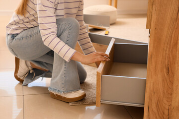 Young woman assembling chest of drawers at home