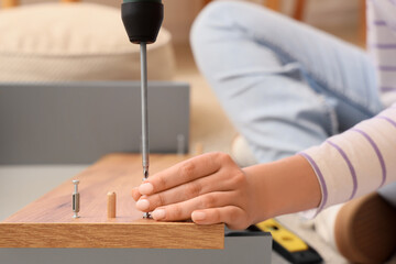 Woman with drill assembling chest of drawers at home, closeup