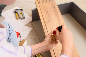 Woman with screwdriver assembling chest of drawers at home, closeup
