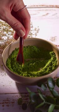 Close up slowmotion of wooden spoon gently stirring vibrant green powder in ceramic bowl. content related to tea, wellness, superfoods in a natural setting. Matcha , Barely gras, Vitamin or Spirulina.