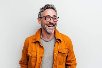Fototapeta premium A joyful middle-aged man with glasses and a grey beard, wearing an orange jacket, is laughing against a white background.