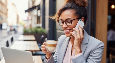 Woman talking on phone while holding a coffee cup near her laptop outside