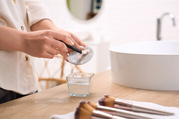 Woman washing makeup brush with tool in bathroom, closeup
