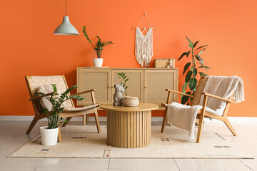 Interior of stylish living room with armchairs, coffee table and wooden cabinet near orange wall