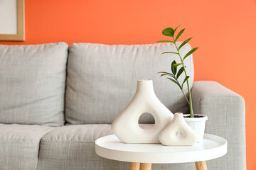 Coffee table with houseplant and vases near grey sofa in stylish living room, closeup