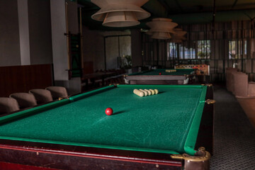Cozy billiard room featuring classic green-felt pool tables; red and white balls arranged for play beneath soft pendant lamps in a modern hotel leisure space