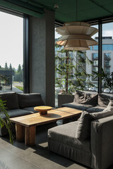 Sun-lit hotel lounge with grey modular sofa, oak coffee table, large potted tree and sculptural...