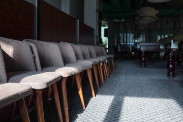 Row of gray upholstered chairs with tapered wooden legs lines a carpeted billiard-lounge corridor; dramatic sunlight and shadows lead the eye toward distant pool tables
