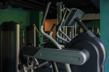 Side view of Technogym elliptical trainer in a dimly lit hotel fitness room with teal walls and other machines in the background, ready for a cardio session, no people present