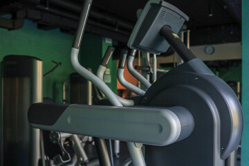 Side view of Technogym elliptical trainer in a dimly lit hotel fitness room with teal walls and other machines in the background, ready for a cardio session, no people present