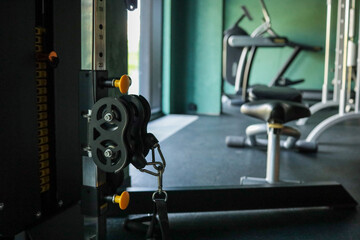 Close-up of an adjustable cable-pulley weight machine in an empty fitness studio; sharp detail on black-and-yellow hardware with cardio gear softly blurred in the background