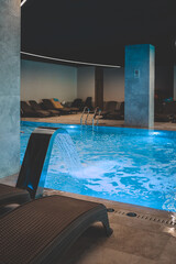 A sleek stainless fountain pours into a luminous blue indoor pool, churning bubbles beneath soft...