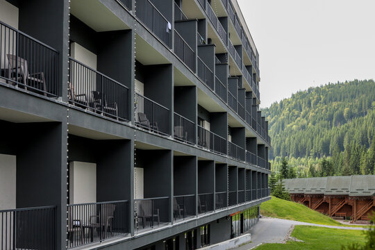 Side view of a modern black-and-white hotel with repeating balcony boxes overlooking a lush forested mountain slope on a summer day in the Carpathians