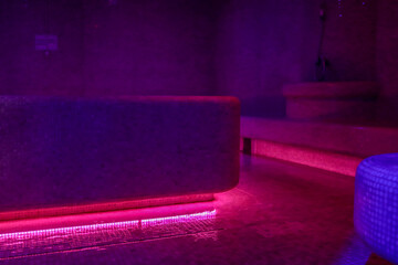 Violet-lit steam room with misty air, mosaic-tiled benches and a glowing heated centerpiece create...
