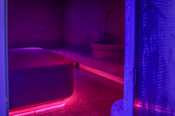 Violet-lit steam room with misty air, mosaic-tiled benches and a glowing heated centerpiece create...