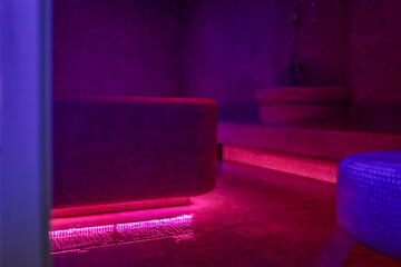 Violet-lit steam room with misty air, mosaic-tiled benches and a glowing heated centerpiece create...
