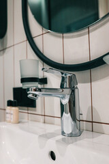 Close-up of shiny chrome single-lever bathroom faucet on white ceramic basin with tiled wall and...
