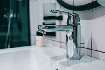 Close-up of shiny chrome single-lever bathroom faucet on white ceramic basin with tiled wall and...