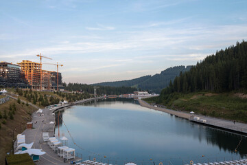 Elevated view of emerald mountain reservoir in alpine resort: calm water mirrors pine-clad slopes,...