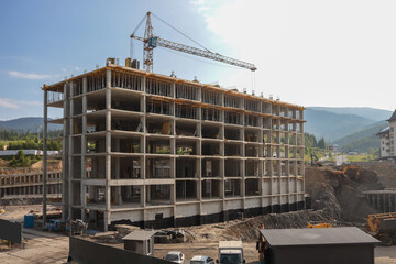 Concrete skeleton of multi-storey building rises beside a tower crane on busy mountain-resort...