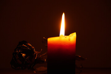 Burning candle and golden rose lying next to it on table at home in darkness, candle