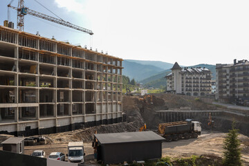 Concrete skeleton of multi-storey building rises beside a tower crane on busy mountain-resort...