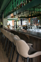 Row of beige leather bar stools along a wooden counter in a stylish modern lounge bar; low-angle perspective highlights sleek interior design and inviting ambience
