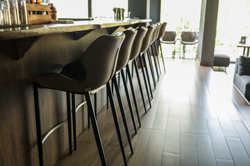 Row of beige leather bar stools along rustic wooden counter in bright modern lounge bar, showing stylish hospitality interior ready for guests