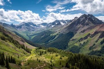 Fototapeta premium Panoramic view of a mountainous valley, lush green slopes dotted with pine trees, snow-capped peaks under a vibrant blue sky with fluffy white clouds