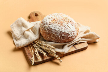 Cutting board with loaf of fresh bread and wheat ears on orange background