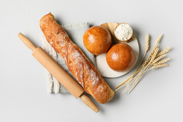 Board with loaf of fresh baguette, buns and flour bread on grey background