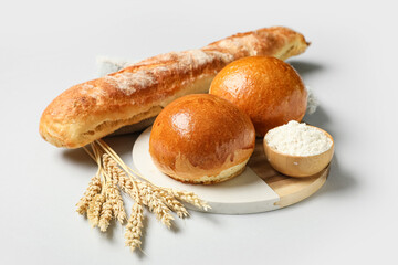 Board with loaf of fresh baguette, buns and flour bread on grey background