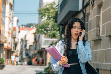 student with books and backpack surprise gesture talking with phone on the street