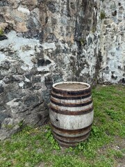 Old wooden barrel placed against a weathered stone wall on grass. Suitable for design, gaming,...