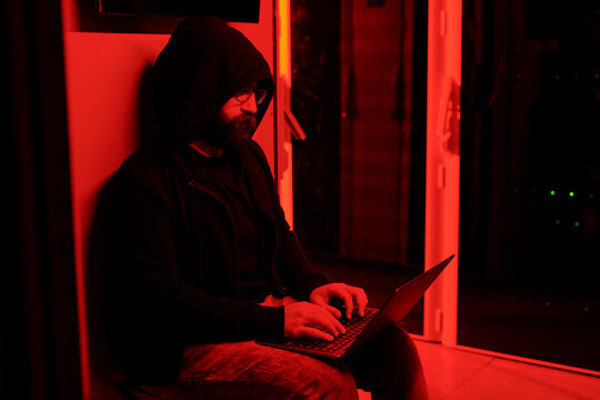 Computer hacker using laptop in server room with red light