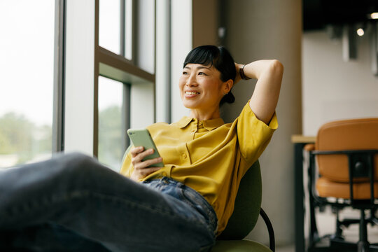 Woman relaxing with smartphone in modern office setting
