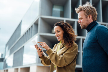 Smiling businesswoman and businessman discussing over tablet PC