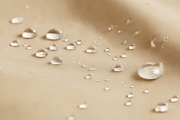 Close-up of water droplets on beige waterproof fabric, showcasing water resistance and texture. Ideal for textile, fashion, or outdoor gear advertising.